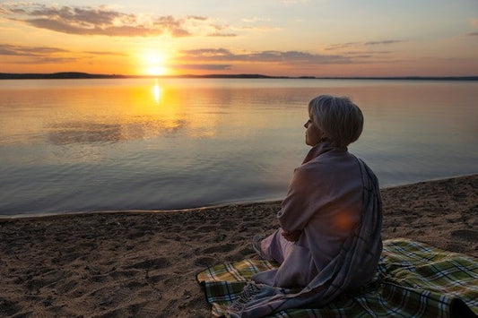 A relaxed older woman on a beach watching a glorious sunset.